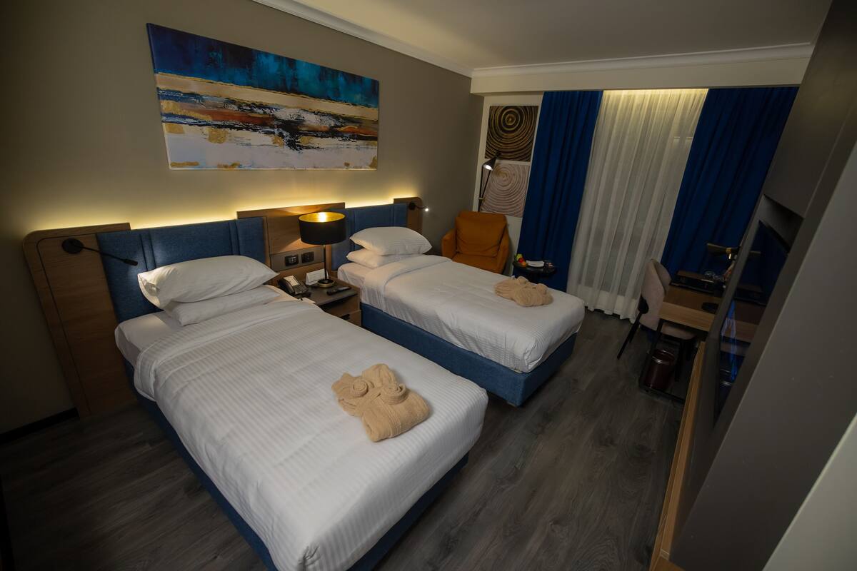 Een hotelkamer met twee bedden, een bureau, een stoel, een lamp en een schilderij aan de muur.