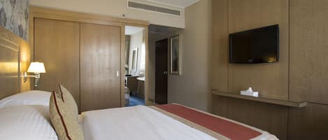 Una habitación de hotel con una cama, un televisor montado en la pared y una puerta que da a un baño.
