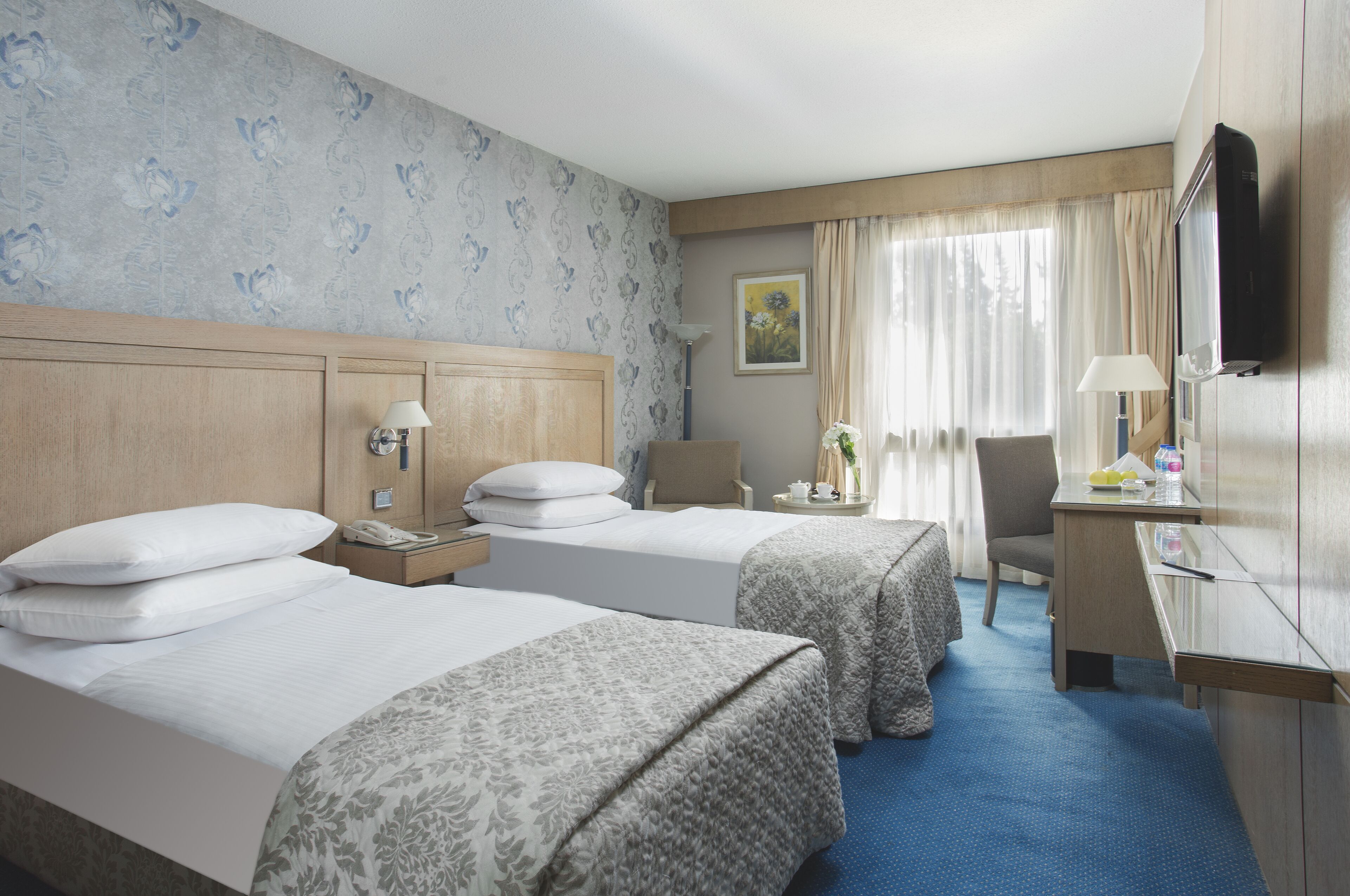 Ein Hotelzimmer mit zwei Betten, einem Schreibtisch, einem Stuhl, einem Fernseher und einem Fenster mit Vorhängen.
