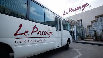 Un autobús blanco con la leyenda 'Le Passage Cairo Hotel & Casino' estacionado frente a un edificio con un letrero grande.
