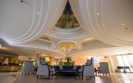 A spacious lobby with a central seating area, a chandelier, and a large window with a view of the sky.