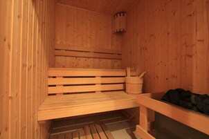 A wooden sauna with a bench, a bucket, and a container of rocks.