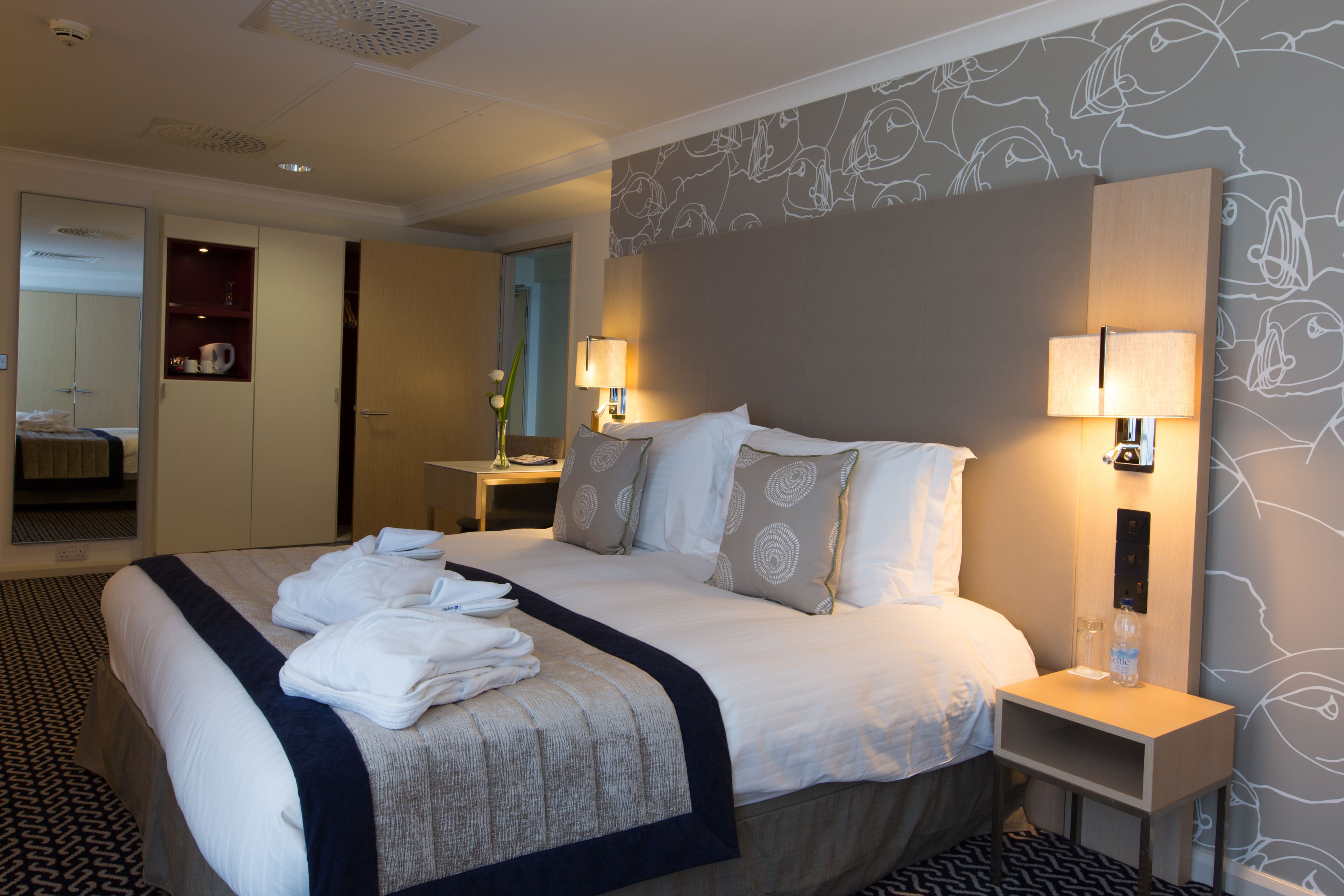 A hotel room with a neatly made bed, bedside lamps, a nightstand, and a mirror.