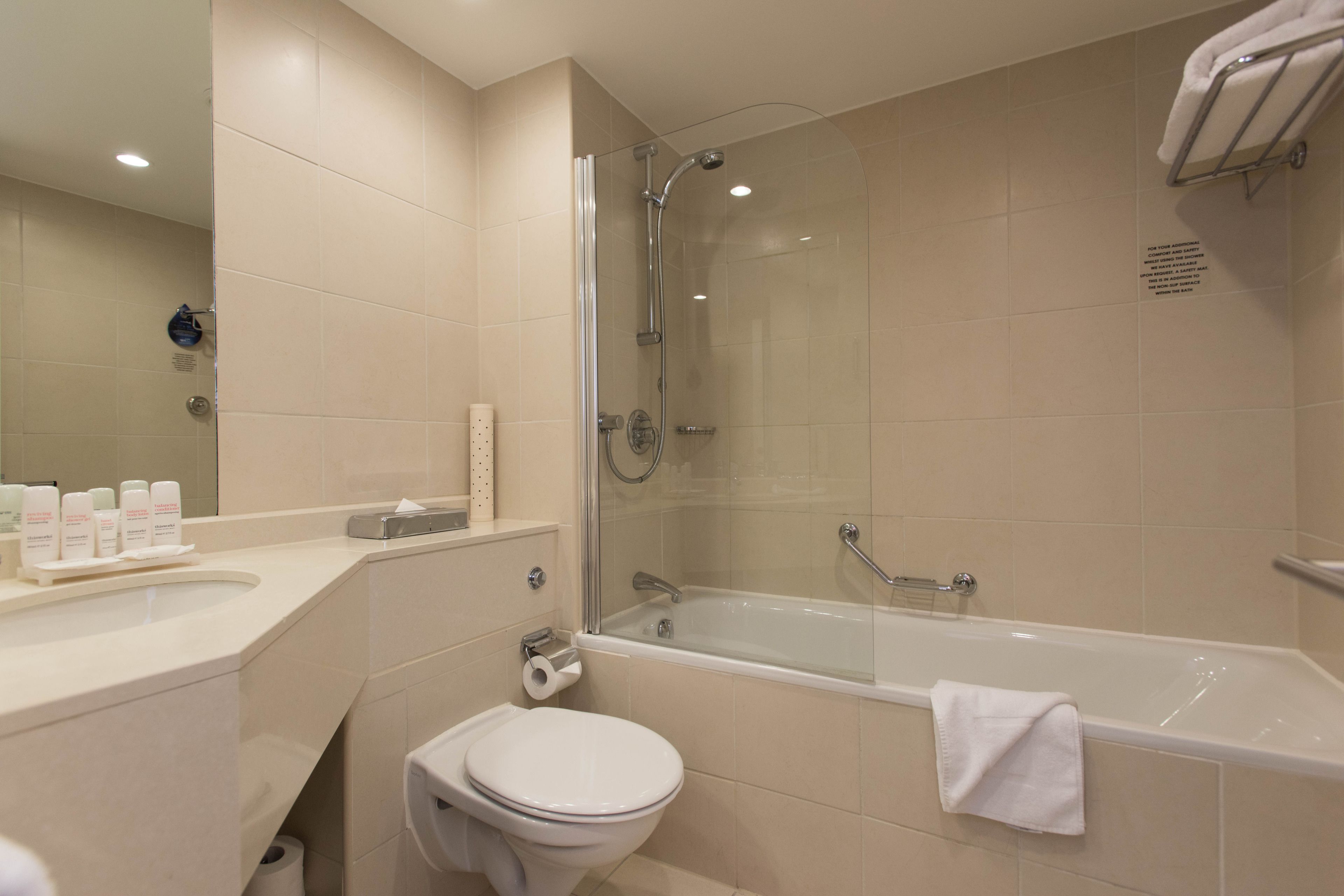 A modern bathroom with a glass-enclosed shower, a bathtub, a toilet, and a vanity with toiletries.