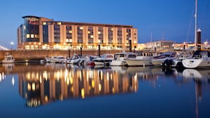 Uma marina com vários barcos atracados em frente a um hotel moderno com vários andares e varandas.