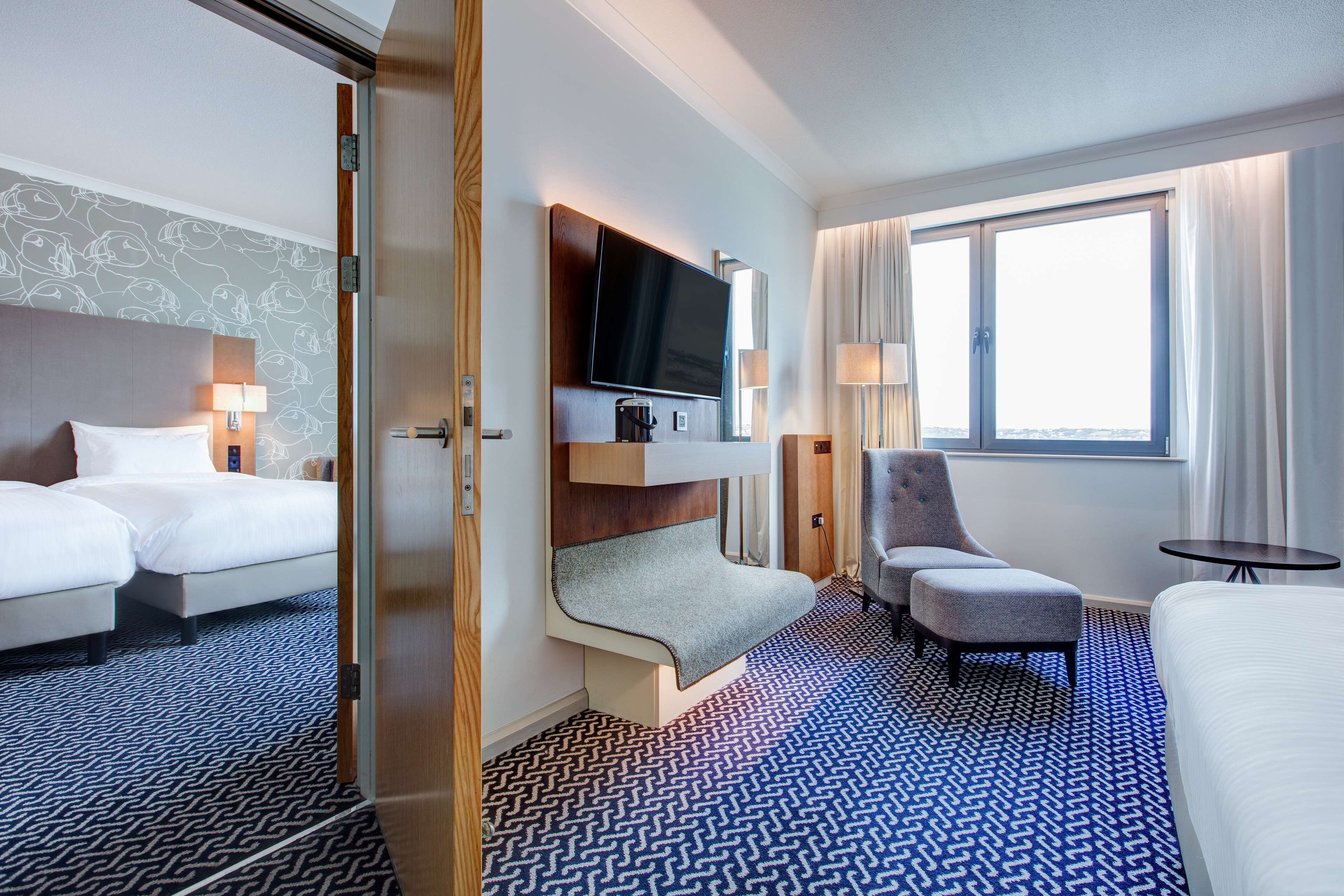 A hotel room with two beds, a TV, a seating area, and a window with curtains.
