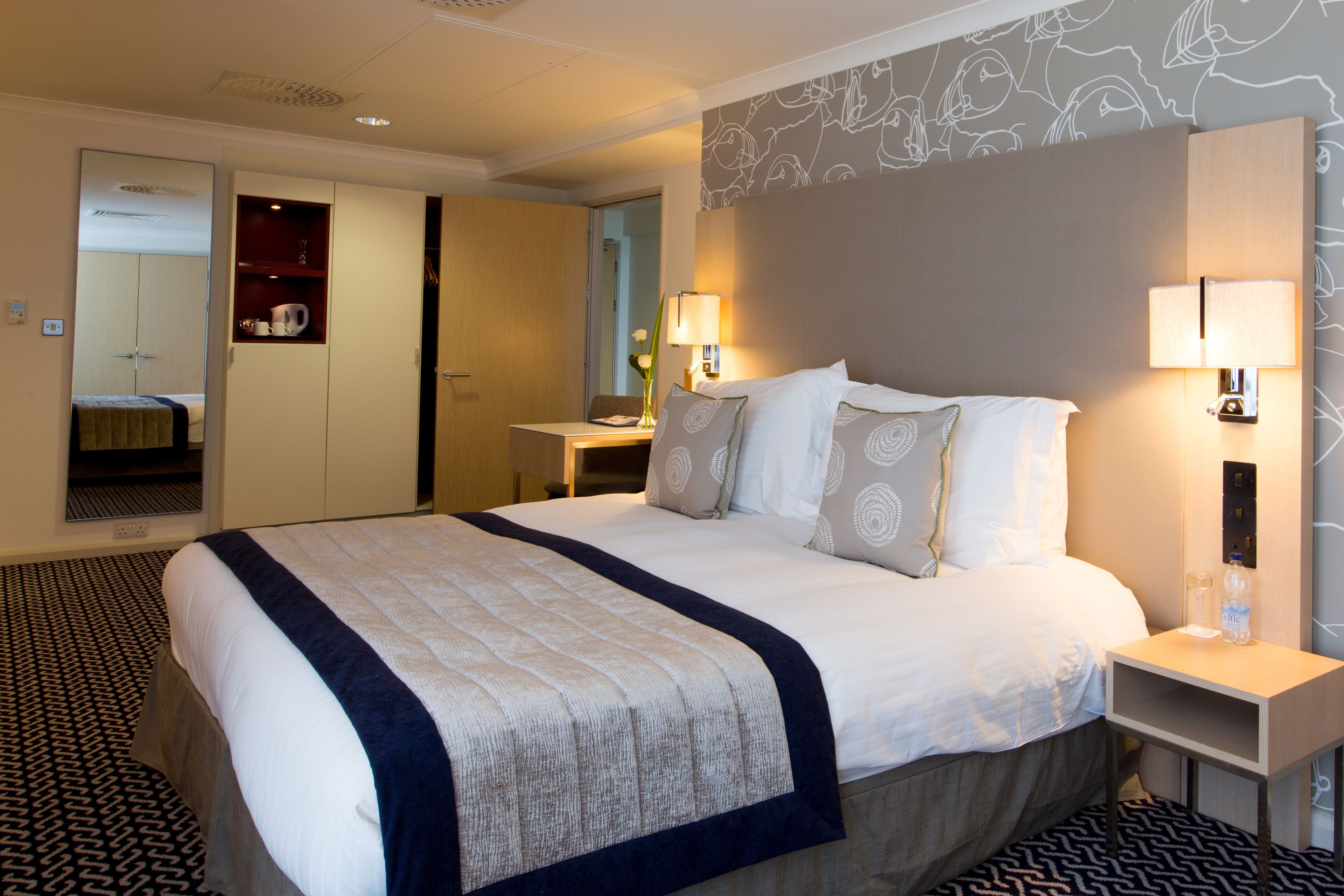 Una habitación de hotel con una cama grande, mesitas de noche, un armario y un espejo.