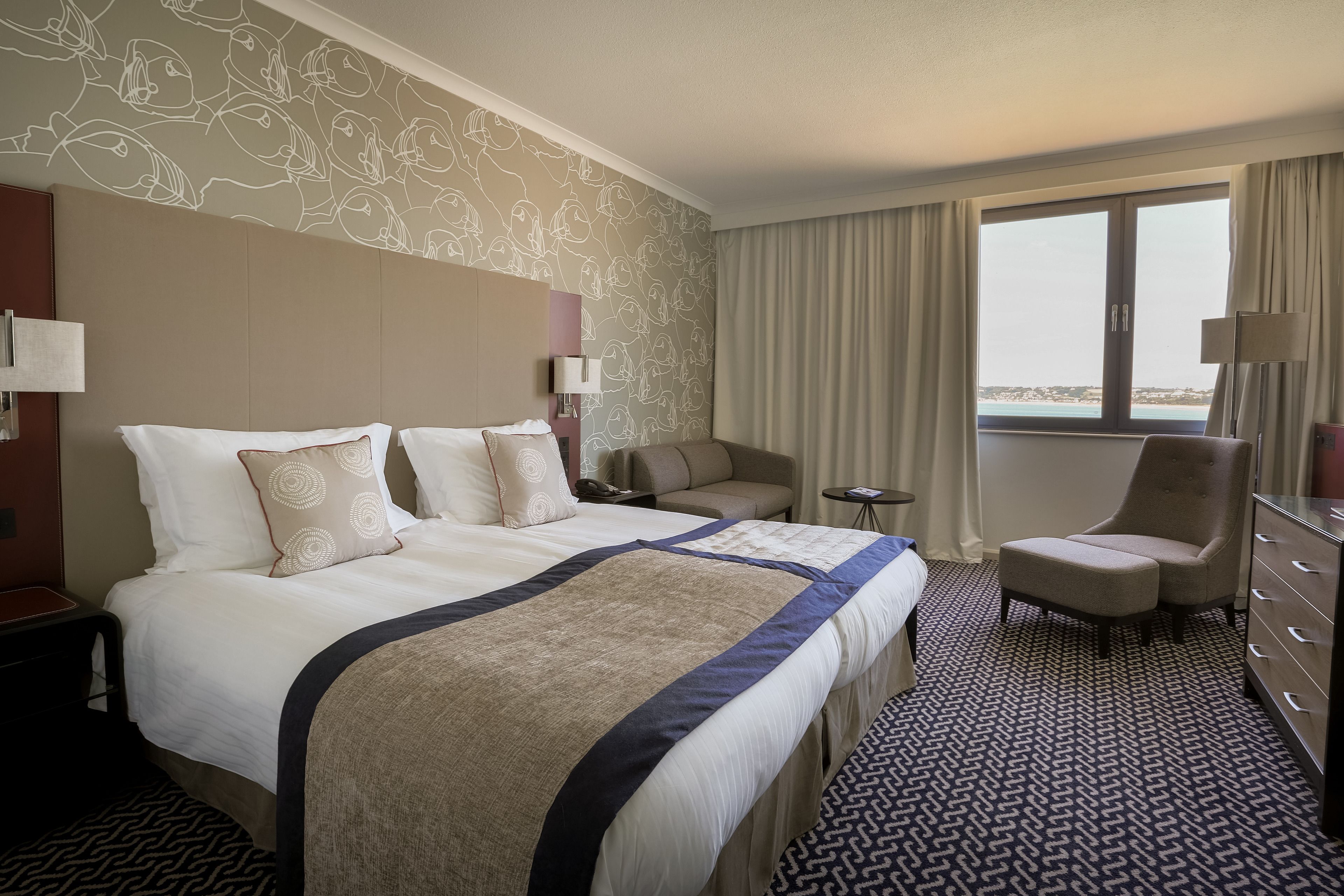 A hotel room with a large bed, a sofa, a chair, a desk, and a view of the sea.