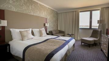 A hotel room with a large bed, a sofa, a chair, a desk, and a view of the sea.