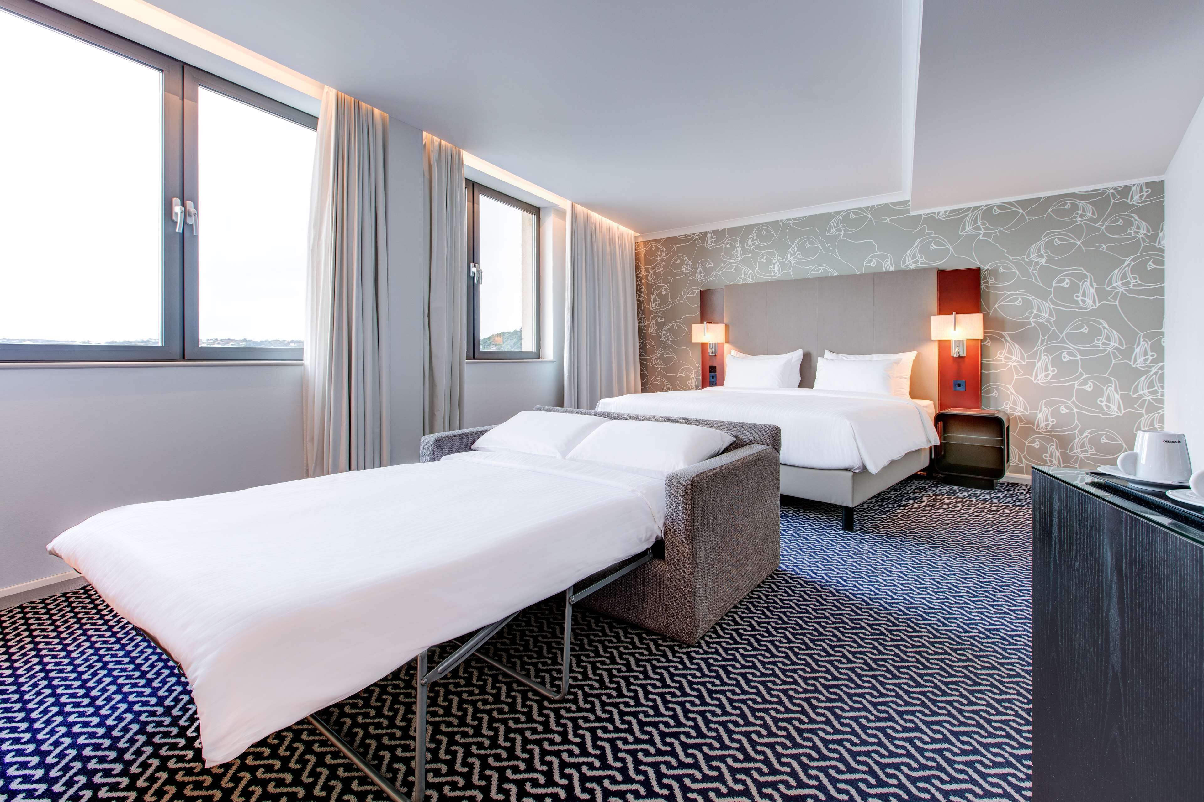 Habitación de hotel con cama, sofá, escritorio y ventana con cortinas.