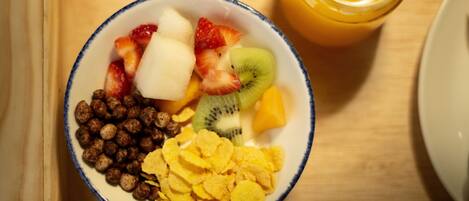 Un tazón de cereal con frutas y un vaso de jugo de naranja sobre una bandeja de madera.