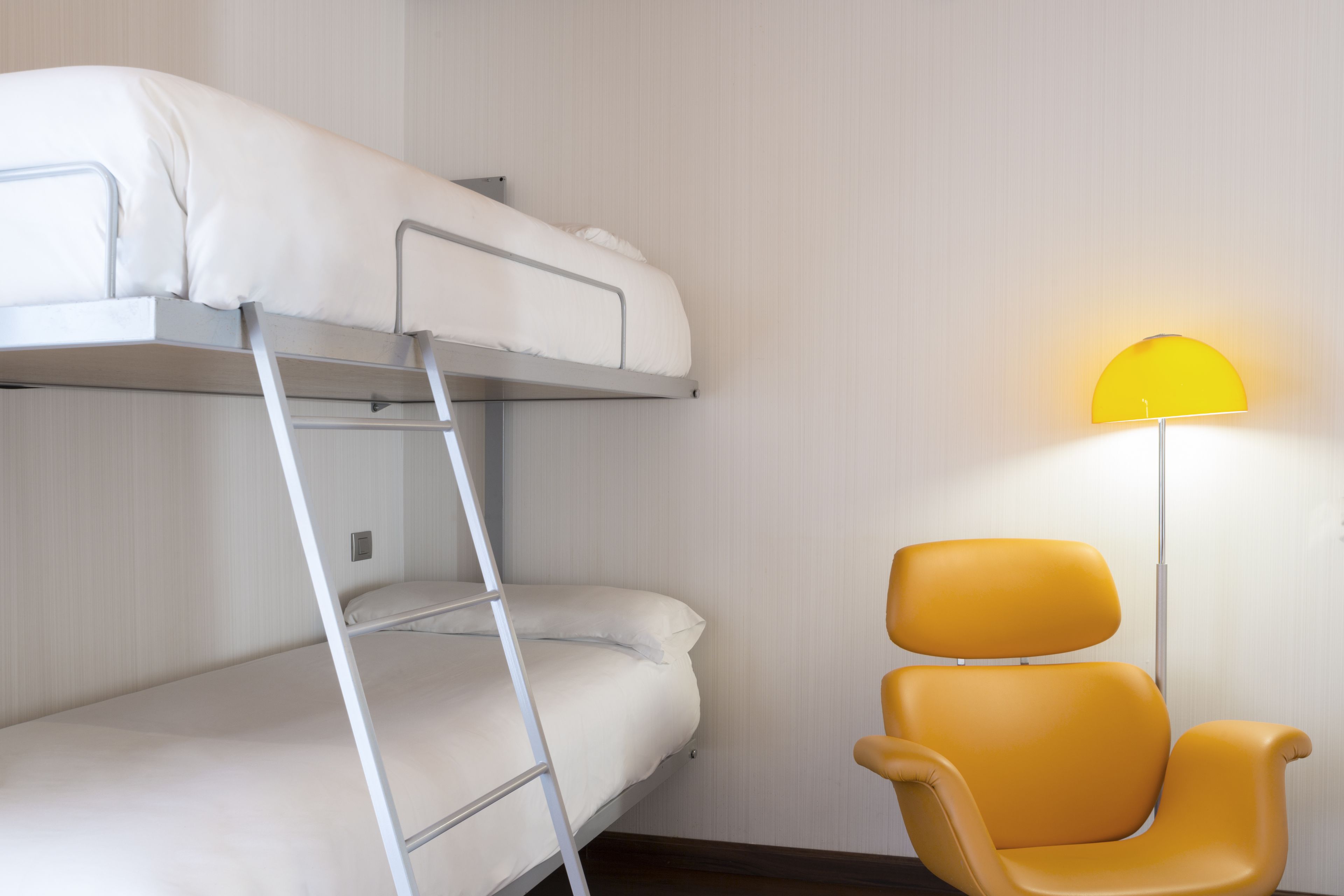 Un lit superposé avec une échelle, une chaise jaune et une lampe fixée au mur.