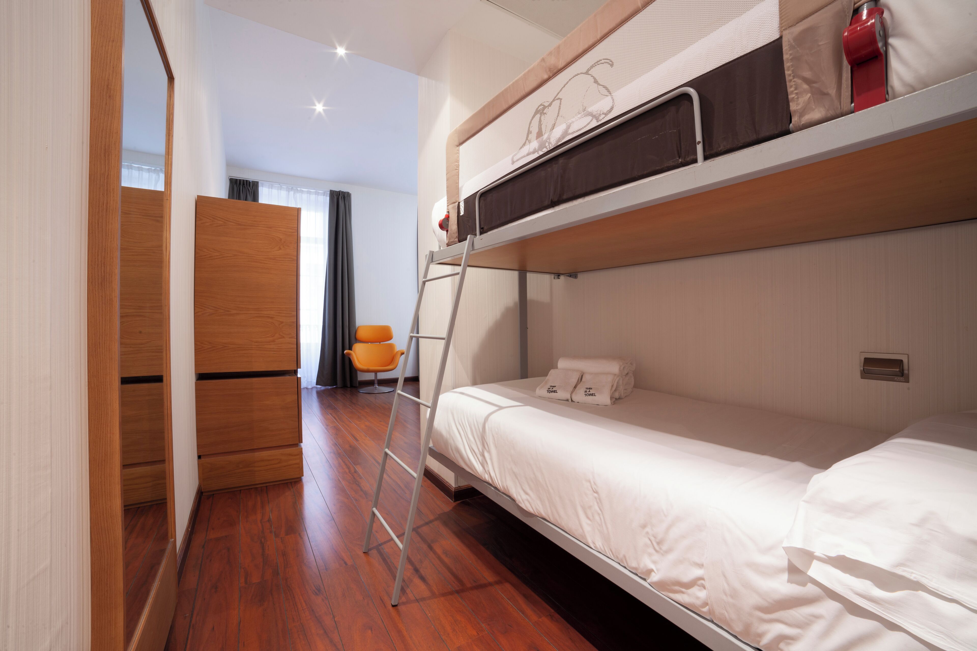 A bunk bed room with a ladder, wooden flooring, a chair, and a wardrobe.