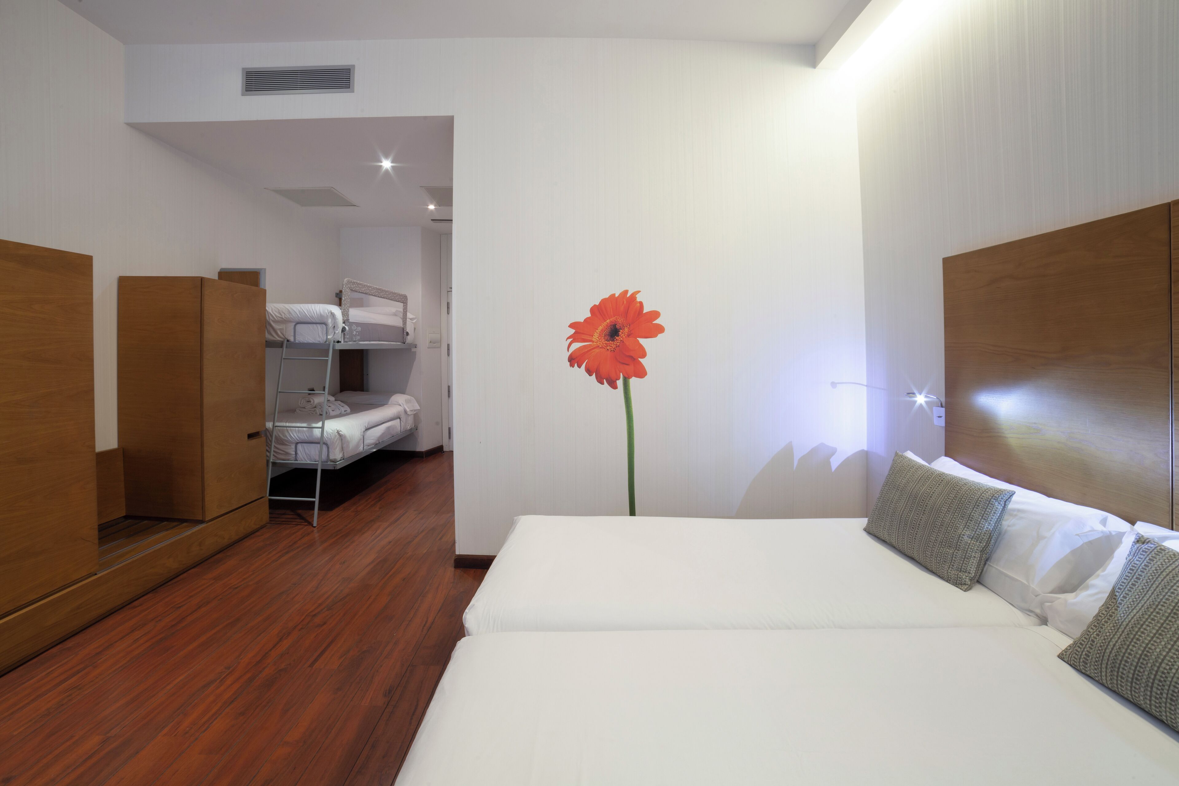 Ein Hotelzimmer mit Etagenbett, einem Einzelbett, Holzmöbeln und einer großen roten Blume an der Wand.