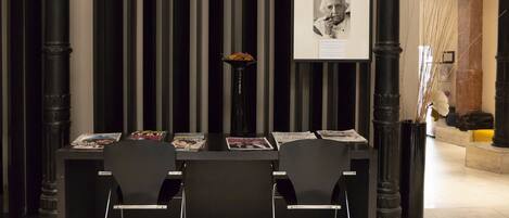 Un espace d’accueil avec un comptoir noir, deux chaises noires, un vase avec des fleurs et un tableau encadré au mur.