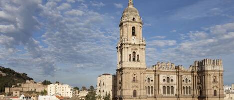 Una catedral histórica con una imponente torre campanario, rodeada de edificios residenciales y un paisaje montañoso.