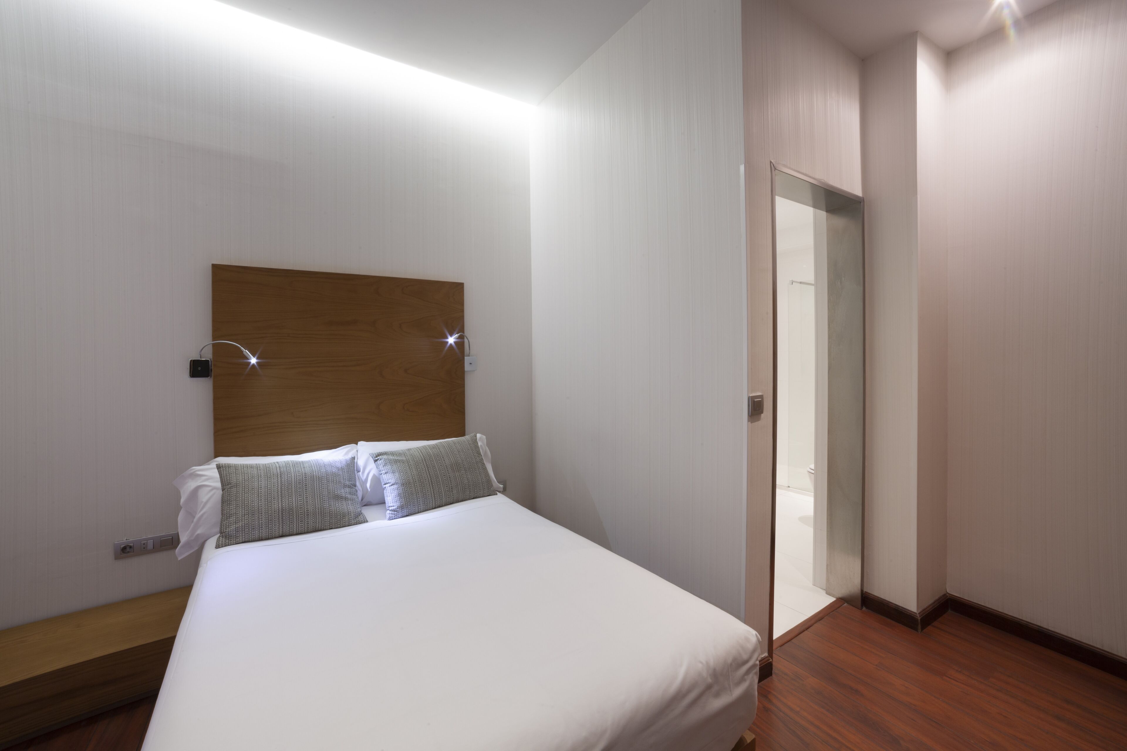 A hotel room with a wooden headboard, a bed with white linens, a bedside table, and a mirror on the wall.