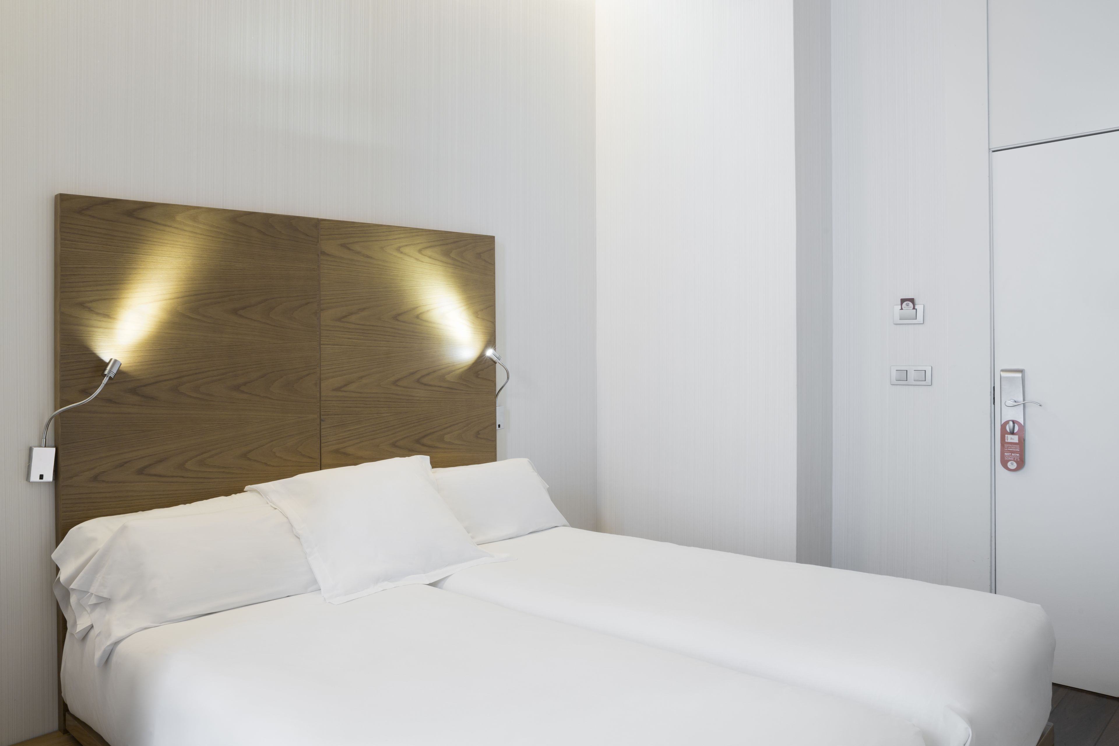 A hotel room with a wooden headboard, white bedding, and a wardrobe with a door lock.
