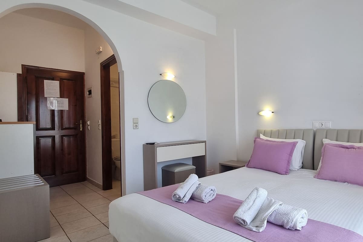 Une chambre d’hôtel avec un grand lit, deux tables de chevet, un grand miroir rond accroché au mur et une porte donnant sur une autre pièce.