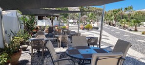 An outdoor patio with wicker furniture, potted plants, and a view of the street. - Horizon Resort (Santorini)