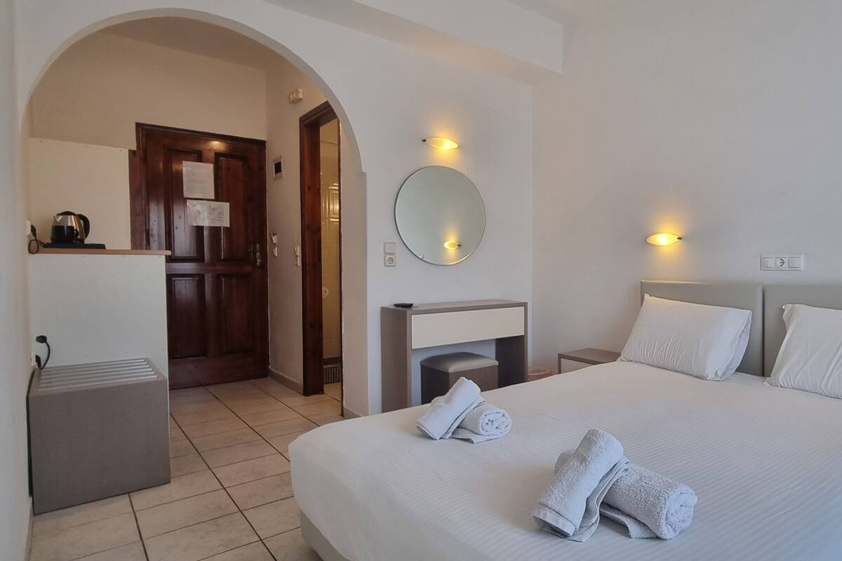 Une chambre d’hôtel avec un grand lit, deux tables de chevet, une commode, un miroir et un petit bureau avec une bouilloire.