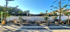 An outdoor patio with tables and chairs, surrounded by potted plants and a white wall. - Horizon Resort (Santorini)
