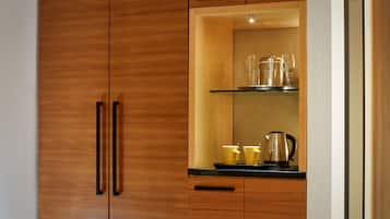 A wooden cabinet with a glass shelf containing a kettle, two cups, and two wine glasses.