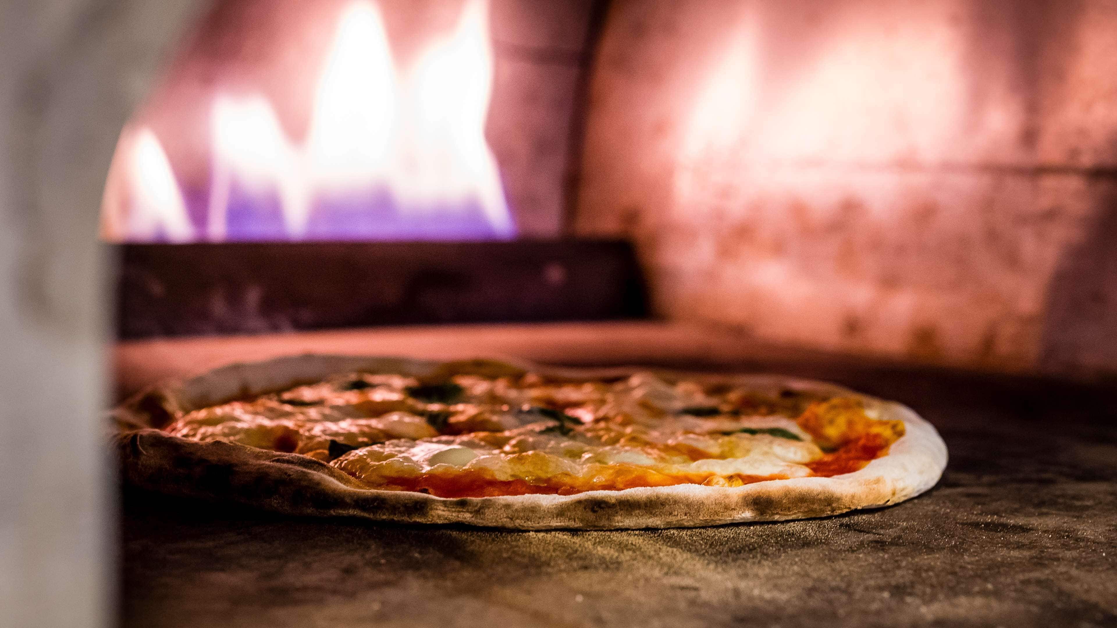 A pizza in a wood-fired oven with visible flames.