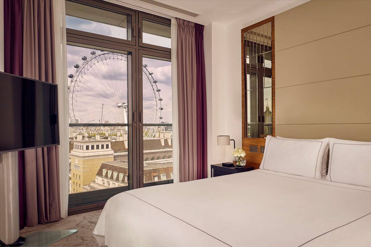 A hotel room with a large bed, a TV, a nightstand, and a view of a Ferris wheel.