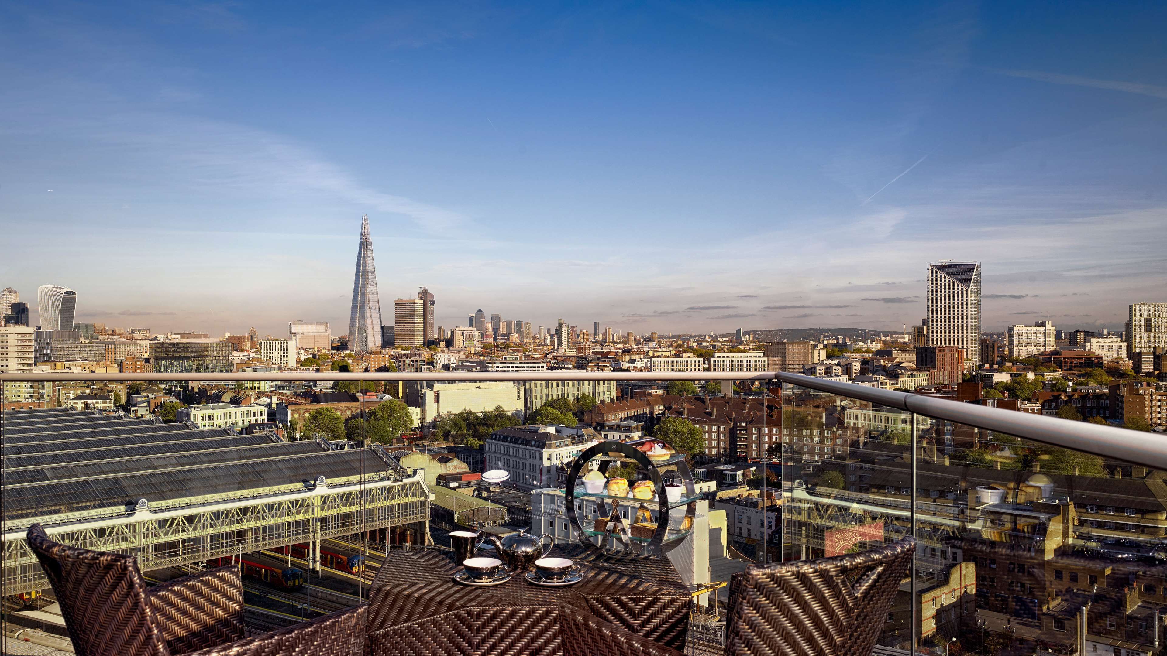 A cityscape with a prominent skyscraper, a bridge, and a railway station with a tea service setup.