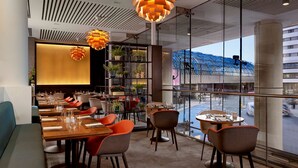 A modern restaurant with a long dining table, multiple chairs, and hanging pendant lights. - Park Plaza County Hall London (London)