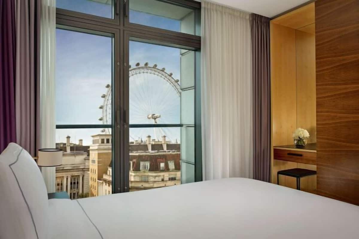 A hotel room with a large window, a bed, a desk, and a chair.