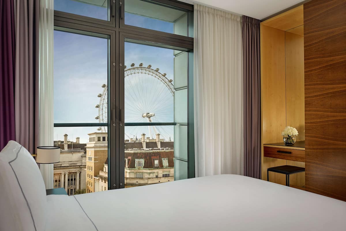 A hotel room with a large window, a bed, a nightstand, and a wooden wardrobe.