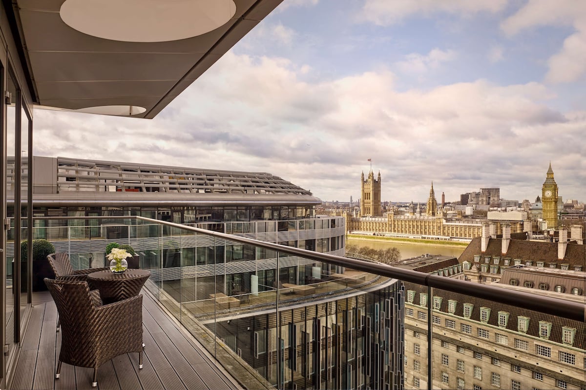 A modern balcony with glass railings overlooking a cityscape, including historic buildings and a river.
