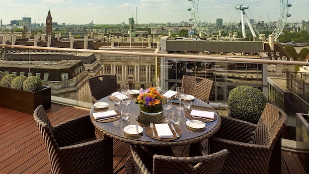 A rooftop dining area with wicker chairs and a round table set for four, overlooking a cityscape with a prominent Ferris wheel. - Park Plaza County Hall London (London)