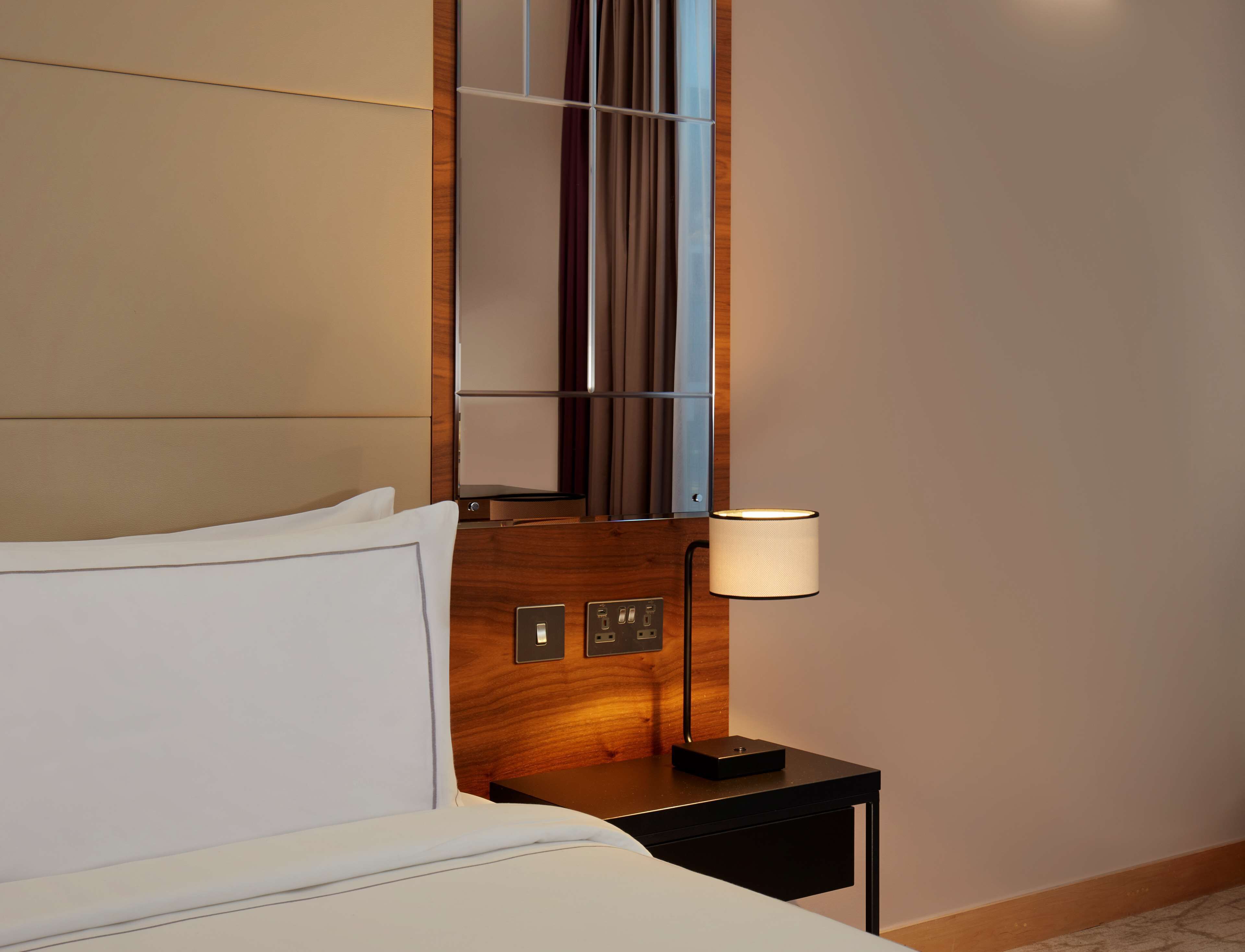 A hotel room with a bed, a nightstand, a lamp, and a mirror.
