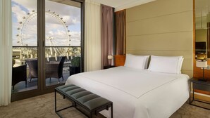 A hotel room with a large bed, a bench, a view of the London Eye, and a balcony with chairs. - Park Plaza County Hall London (London)