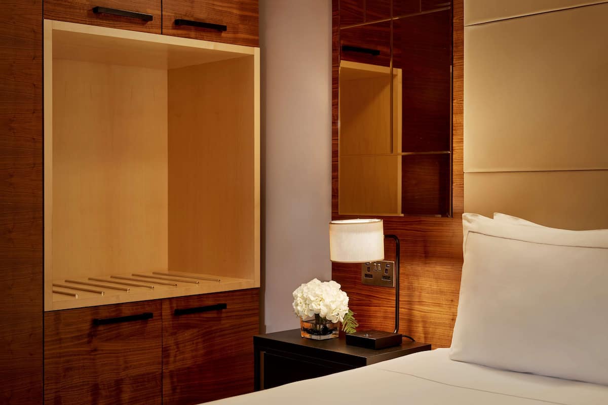 A hotel room with a large wardrobe, a bedside table with a lamp, and a bed with a white pillow.