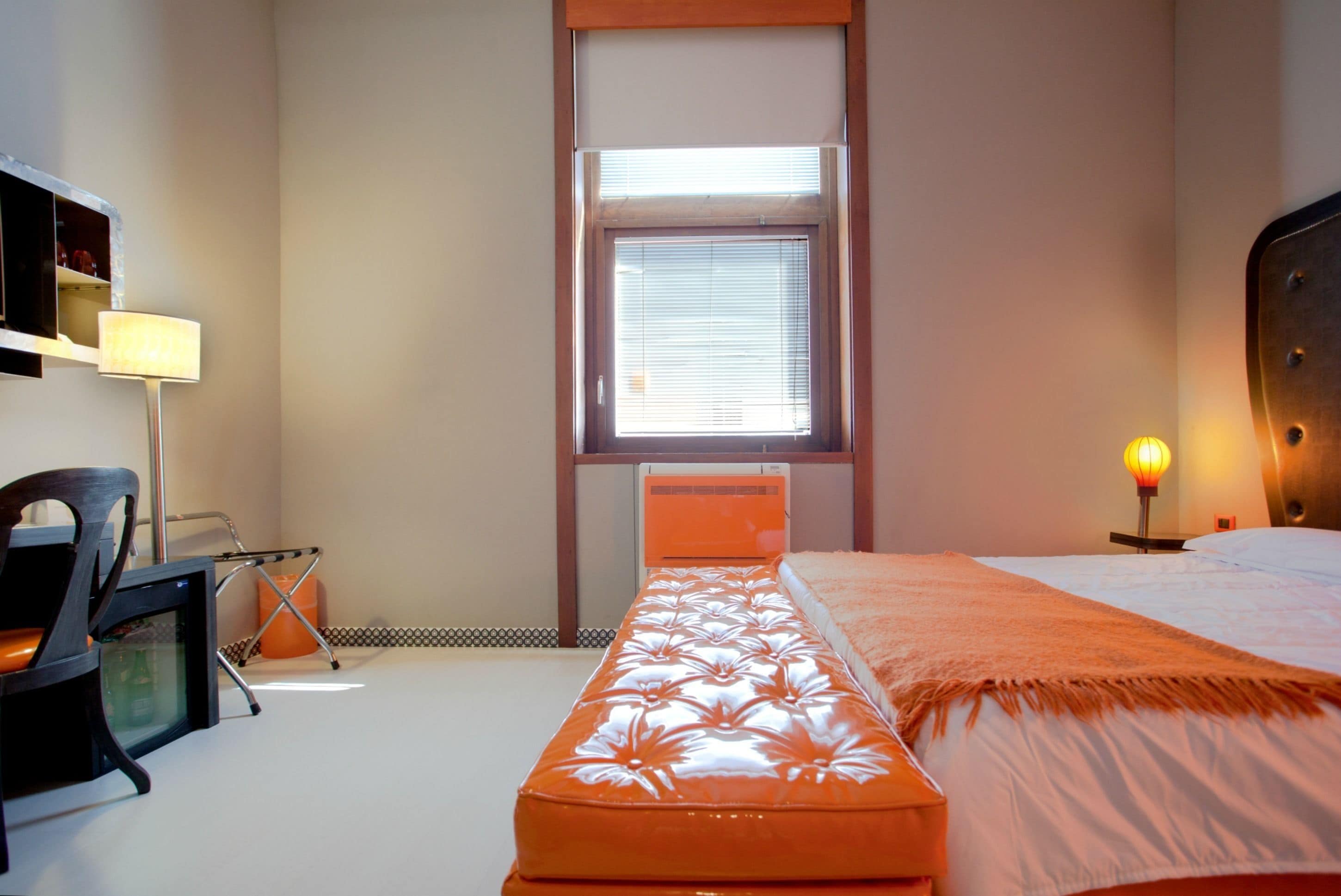 Ein Schlafzimmer mit Bett, Schreibtisch, Stuhl, Fenster mit Jalousien und Heizung.