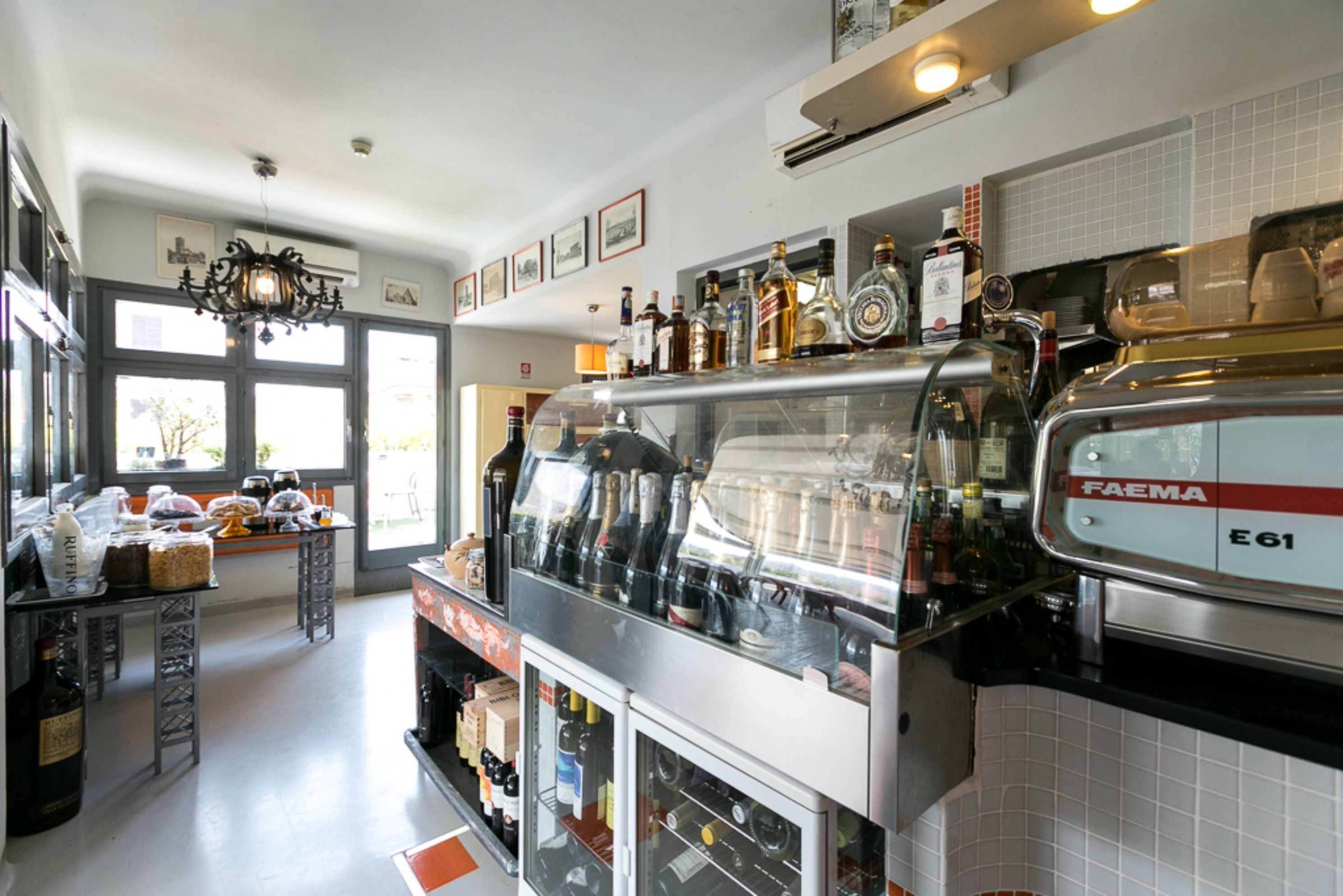A kitchen with a coffee machine, shelves with bottles, and a window with a view.