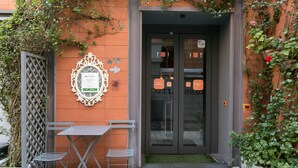 A building entrance with a glass door, a small outdoor seating area with a table and chairs, and a decorative mirror on the wall. - Orange Hotel (Rome)