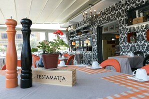Un restaurante con terraza, un letrero de madera que dice "TESTAMATTA" y una planta en maceta sobre la mesa.