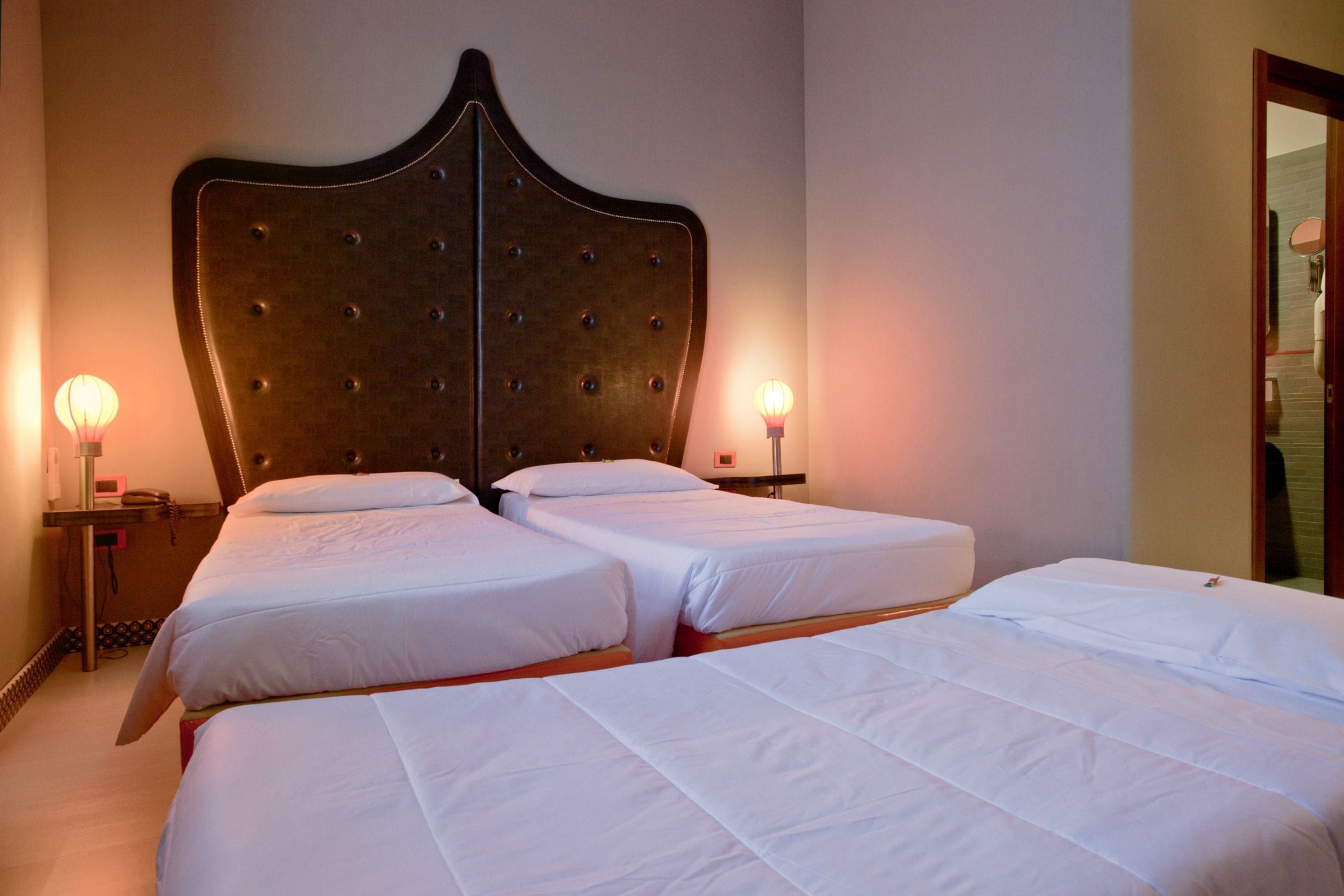 Habitación de hotel con dos camas, un cabecero grande, lámparas de noche y un espejo.