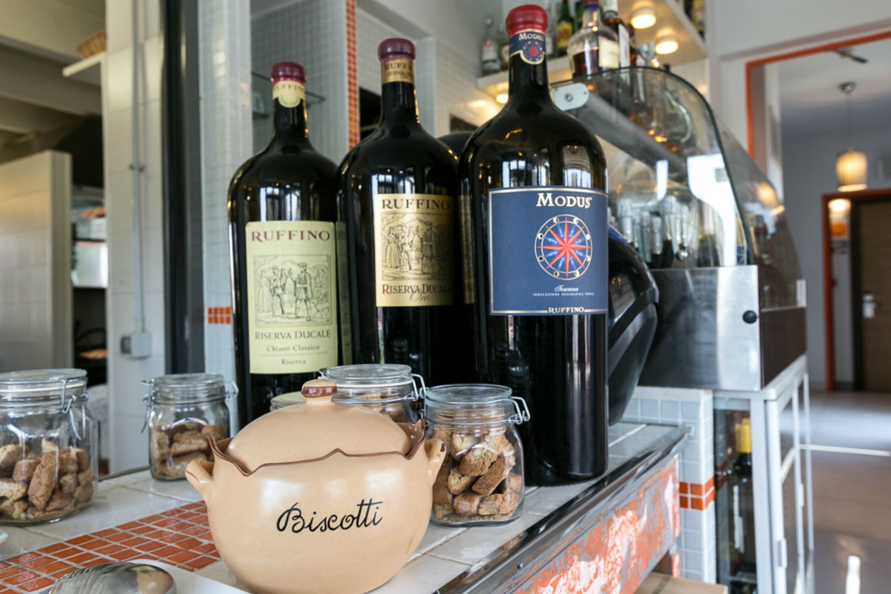 A bar counter with bottles of wine and jars of biscotti.