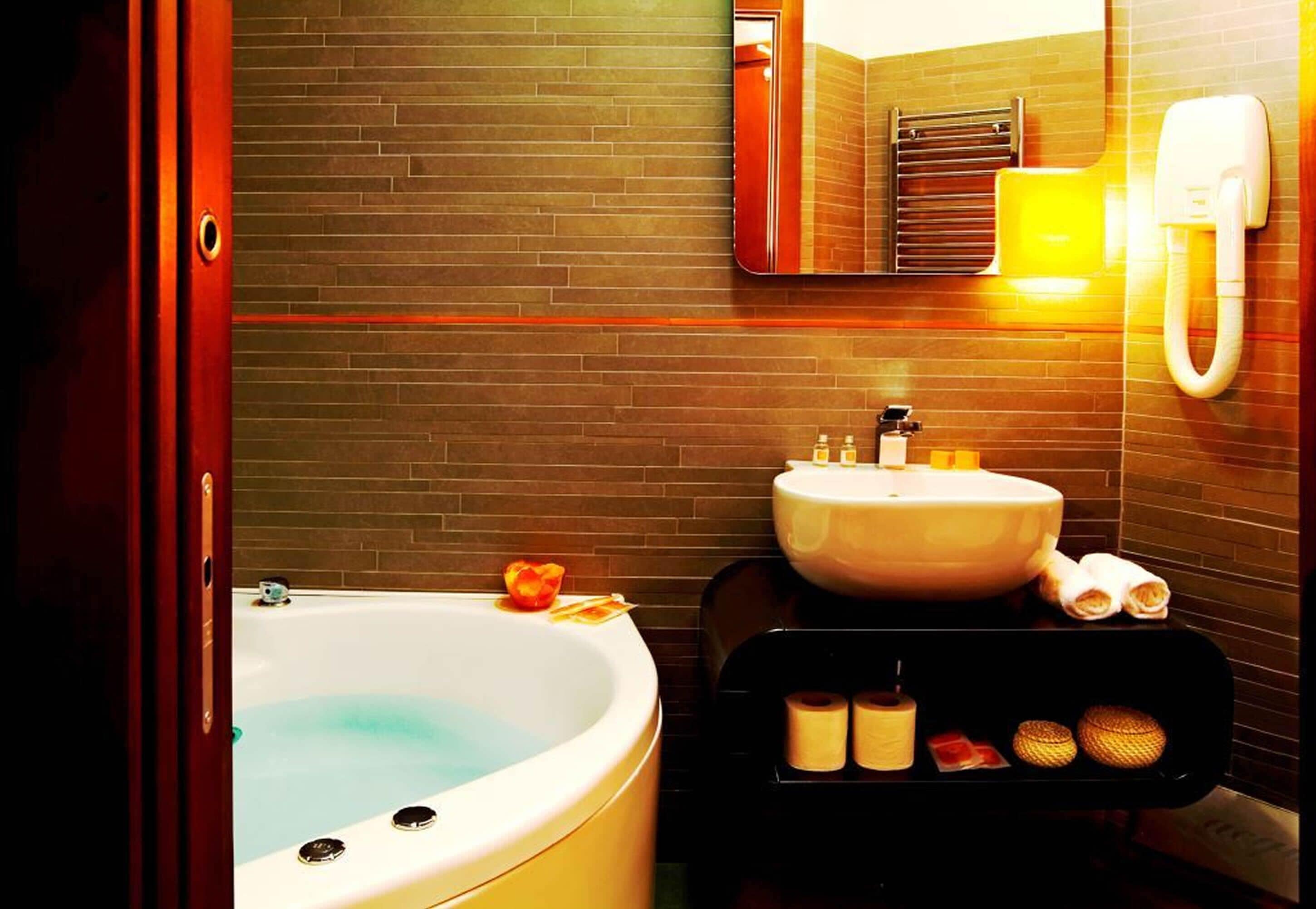 A bathroom with a large bathtub, a sink, and a mirror. There are toiletries on the sink and a towel rack.