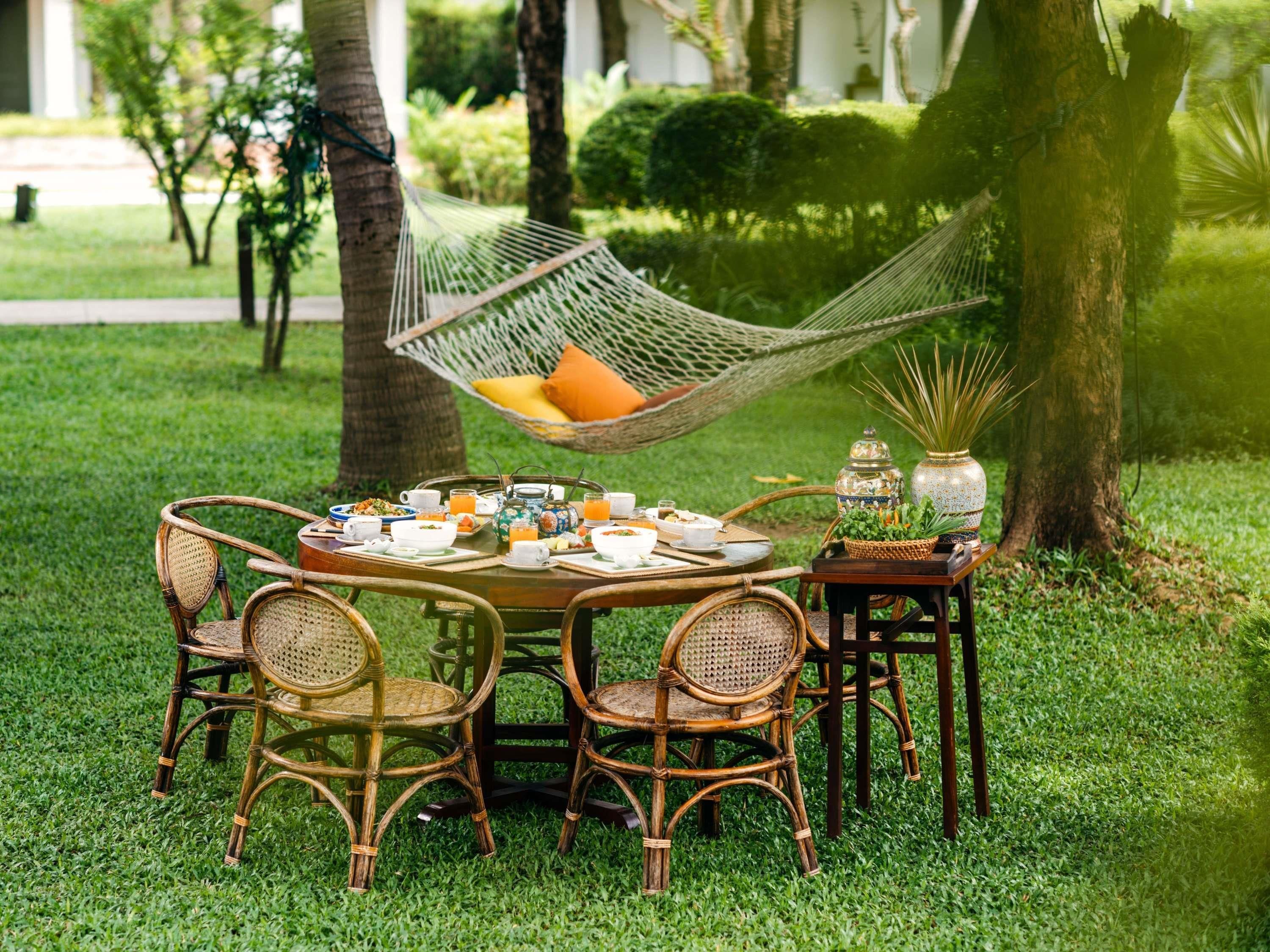 Une table ronde entourée de chaises en osier, un hamac et une petite table agrémentée d’objets décoratifs.