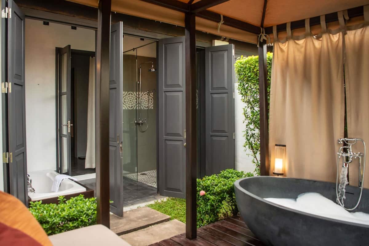 A modern outdoor bathroom with a bathtub, shower, and glass doors leading to a shower area.