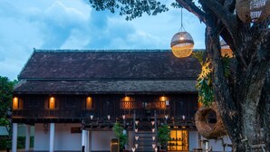 A traditional building with a thatched roof, a wooden facade, and a well-lit entrance. - Sofitel Luang Prabang (Luang Prabang)
