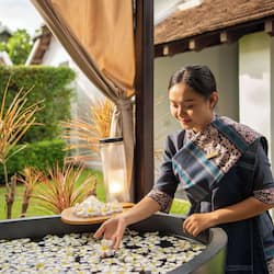 Staff member tends to a serene garden water feature surrounded by lush greenery.