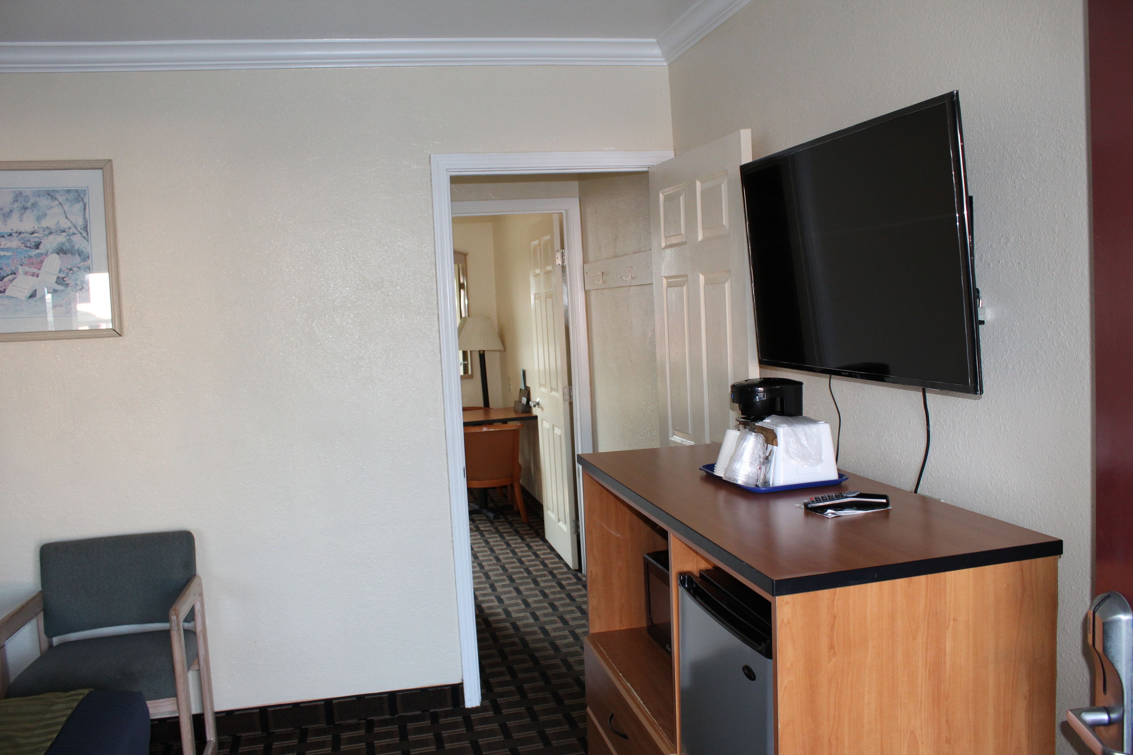 A hotel room with a wooden desk, a television mounted on the wall, a chair, and a door leading to a bathroom.